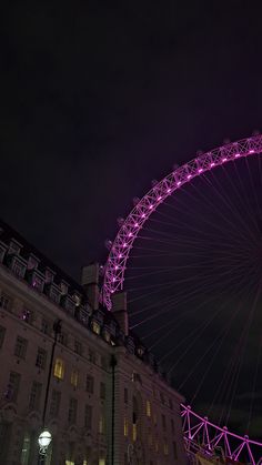 the large ferris wheel is lit up in purple lights on top of it's structure