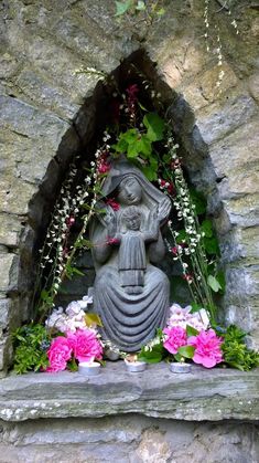 a statue with flowers around it in front of a stone wall and window sill