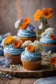 cupcakes with blue frosting and orange flowers on a wooden tray next to a vase