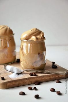 two jars filled with peanut butter sitting on top of a cutting board next to coffee beans