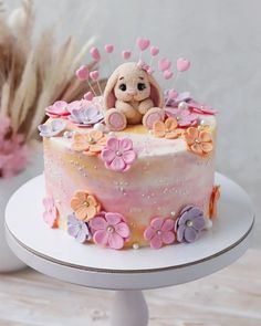 there is a cake decorated with flowers and a teddy bear on top, sitting on a stand