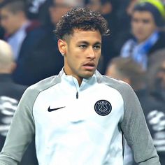 a man with curly hair wearing a white shirt and black pants in front of a crowd