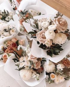 several bouquets of flowers sitting on top of white napkins with greenery around them