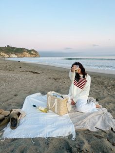 a woman sitting on top of a blanket near the ocean