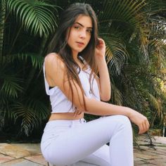 a young woman sitting on the ground in white pants and cropped tank top with her hands behind her head