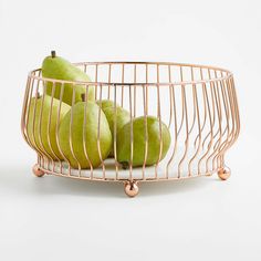 some green pears in a metal bowl on a white surface with gold wire around it