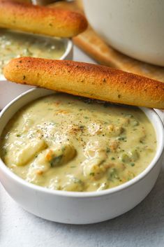 two white bowls filled with soup next to breadsticks and a bowl of dip