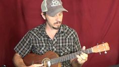 a man playing an acoustic guitar in front of a red curtain with his hat on