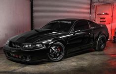 a black mustang parked in front of a garage door with red light coming from behind it