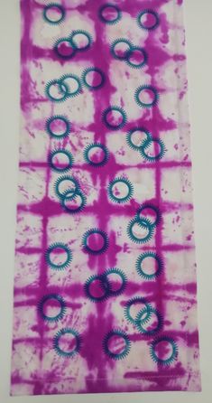 a purple and blue tie - dyed piece of cloth with circles on the side, in front of a white wall