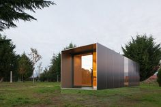 a small building sitting on top of a grass covered field next to trees and bushes