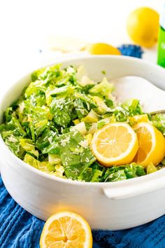 a salad with lemons and lettuce in a white bowl on a blue towel