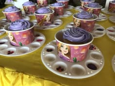 some cupcakes with purple frosting on them are sitting on trays in front of a yellow tablecloth