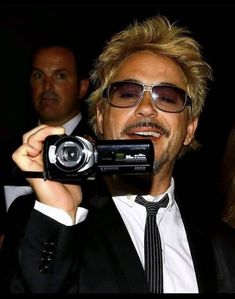 a man in a suit and tie holding up a camera to take a selfie