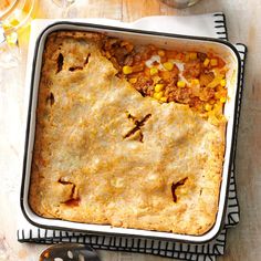 a casserole dish with corn and meat in it sitting on a table next to utensils