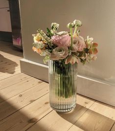 a vase filled with lots of flowers on top of a hard wood floor next to a wall