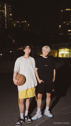 two young men standing next to each other with a basketball in their hands at night