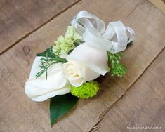 a boutonniere with white flowers and greenery on a wooden table top