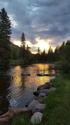 the sun is setting over a river with rocks in it and trees on both sides