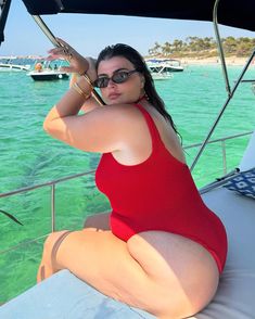 a woman in a red swimsuit is sitting on a boat and posing for the camera