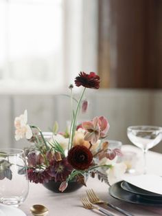 an arrangement of flowers in a vase on a table with silverware and wine glasses