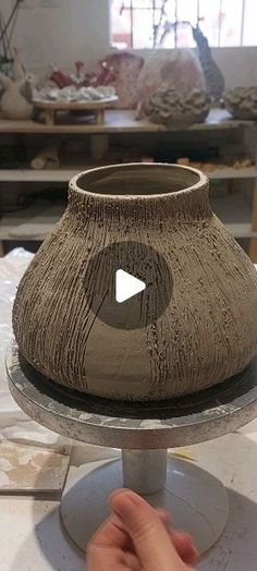 a clay vase being made on top of a metal stand in a pottery shop, with one hand touching the base