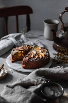 a cake sitting on top of a white plate next to a tea pot and spoon