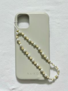 a white phone case with pearls and a gold chain on the back of it, sitting on a white surface