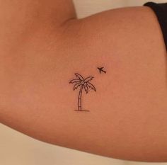 a small palm tree tattoo on the back of a woman's left arm with an airplane flying over it