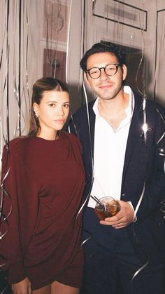 a man and woman standing next to each other in front of streamers holding drinks