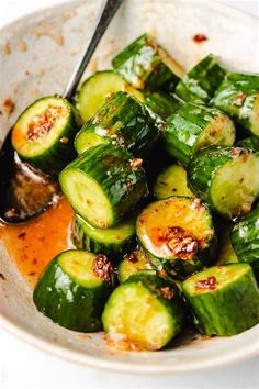 a white bowl filled with sliced cucumbers and sauce on top of a table