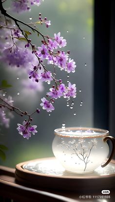 a tea cup and saucer on a table with purple flowers in the window sill