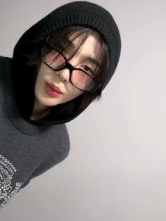 a person wearing glasses and a hoodie posing for a photo in front of a white wall