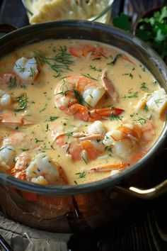 a pot filled with shrimp and cheese soup on top of a wooden table next to bread