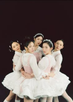 four young ballerinas in white tutus posing for a photo with their arms around each other