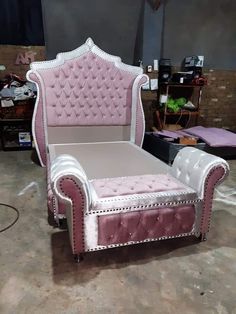 a pink and white bed sitting on top of a floor next to a chair with studded trim