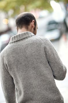 a man walking down the street with his back to the camera, wearing a gray sweater