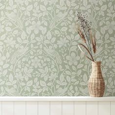 a vase with some flowers in it on a shelf next to a wallpapered wall