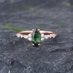 a green and white diamond ring sitting on top of a black stone slab with leaves