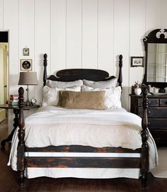 a bedroom with white walls and wood floors has a large bed, two nightstands, and a mirror on the wall