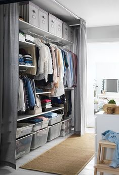 an organized closet with clothes hanging on the walls and plastic bins in front of it