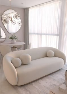 a white couch sitting in front of a window next to a table and mirror on the wall