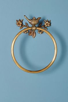 a gold ring with a bird on it and leaves attached to the side, against a blue background