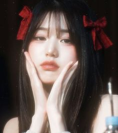 a woman with long black hair wearing a red bow around her head and holding her hands to her face