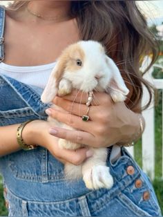 a woman holding a small rabbit in her hands and looking at the camera while wearing overalls