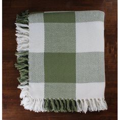 a green and white checkered blanket laying on top of a wooden floor with fringes