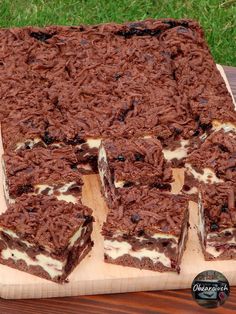 a chocolate cake with white frosting on a wooden cutting board next to some green grass