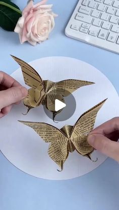 two hands are holding origami birds on top of a white plate with pink flowers