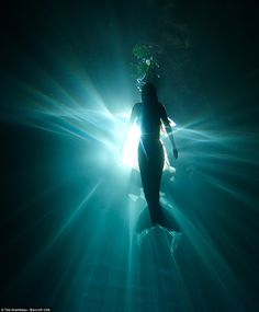 a person standing in the middle of water with their head turned to the side and light shining on them