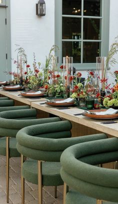 a long table is set with green chairs and flowers in vases on the tables